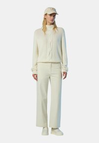 Maglione bianco a trecce con colletto alto, abbinato a pantaloni bianchi a gamba larga. Completato con un cappello crema e sneakers bianche.
