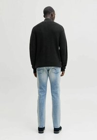 Maglione nero lavorato a maglia con texture a coste, abbinato a jeans azzurri a gamba dritta e scarpe nere, visto da dietro.