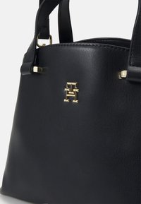 Black leather handbag with gold hardware, featuring a prominent logo and structured shape. Short handles, smooth texture, and sleek design.