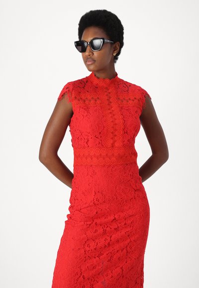 Rochie roșie din dantelă, cu mâneci scurte, de model înalt și un model floral complicat. Model purtând ochelari de soare negri cu formă de pisică. Siluetă netedă și ajustată.