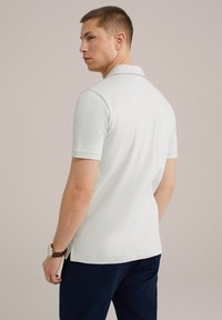 Svetlo sivo polo majica s kratkimi rokavi, ovratnikom in bočnimi razporki. Utežena z mornarskimi hlačami, na zapestju pa je rjav športni uri.