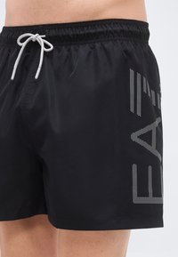 Μαύρα μαγιό σορτς από ελαφρύ υλικό. Διαθέτουν ελαστική μέση με κορδόνι και αντανακλαστικό σχέδιο στη μία πλευρά.