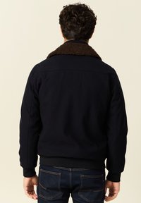 Granatowa kurtka bombowiec z brązowym kołnierzem z polaru, ściągaczami przy mankietach i dolnej krawędzi oraz gładką fakturą materiału. Widok z tyłu pokazuje pełne pokrycie pleców.