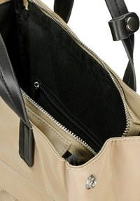 Beige handtas met zwarte leren accenten. Bevat een ritsvak aan de binnenkant en een ruime hoofdcompartiment gevoerd met zwarte stof.