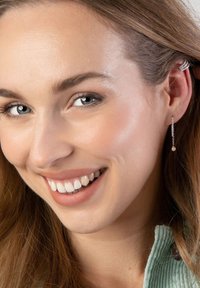 Boucles d'oreilles en argent avec un accent perlé, présentant un design délicat en chaîne. Le modèle a de longs cheveux bruns, des yeux bleus et un sourire.