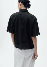 Black short-sleeve shirt made of lightweight fabric, featuring a collar and loose fit. Details include a subtle texture and a straight hem.
