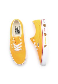 Baskets en toile jaune avec des lacets blancs, dotées d'une semelle rouge et blanche. Des décorations graphiques représentant des aliments sont présentes sur le côté.
