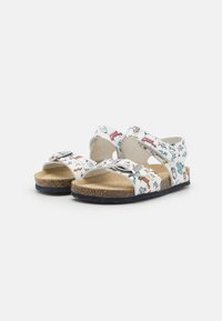 Hvite sandaler med fargerike tegneseriemønstre, justerbare stropper, korksåle og mørk såle. Åpen tå-design for god ventilasjon.