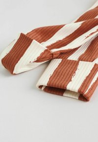 Soonik kangas laiade horisontaalsete triipudega roostepunas ja valkjashallil, voltis heledal hallil pinnal.