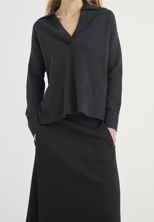 Pull en tricot gris foncé avec un col en V et un col, doté de manches longues et d'une coupe décontractée. Associé à une jupe noire ajustée.