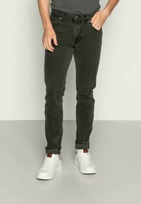 Dark green slim-fit jeans with a five-pocket design, cuffed hems, and a mid-rise waist paired with white sneakers and a grey shirt.