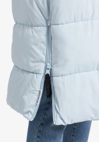 Ljusblå puffjacka med vertikal dragkedja på sidan, med en slät, glänsande yta och en avslappnad, klumpig design.