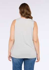 Top senza maniche grigio chiaro in morbido tessuto, con scollatura rotonda e fit rilassato. Indossato con jeans blu, design minimalista.