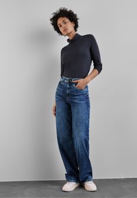 Marinblå mock turtleneck topp kombinerad med vida blå denimjeans. Skorna har accentfärger i rosa och ljusbeige. Släta texturer, avslappnad passform.