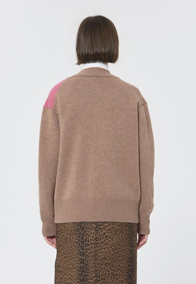 Cardigan tricotat maro cu un accent roz pe umăr și manșete cu nervuri, asortat cu o fustă cu imprimeu leopard. Material texturat, croială lejeră.