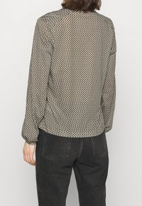 Langärmlige Bluse mit Kragen in Olivgrün und einem weißen Punktmuster, aus leichtem Material gefertigt. Verfügt über einen lockeren Schnitt und leicht geraffte Manschetten.
