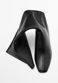 Borsa nera in pelle con un design unico piegato, base quadrata, texture liscia e forma minimalista. Nessuna ferramenta visibile.