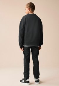Sort oversized sweatshirt med lange ærmer, parret med matchende slim-fit bukser. Fodtøjet har sorte og hvide designelementer.