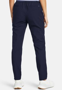 Mørkeblå sportbukser med elastisk talje, slim fit og to baglommer. Båret med hvide sneakers.