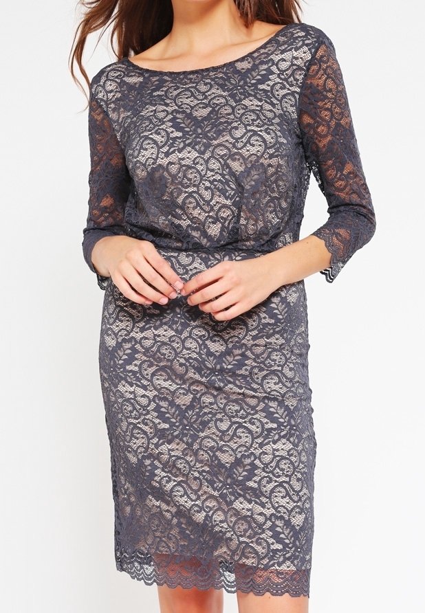 Femme portant une robe en dentelle grise ajustée longueur genou, avec des manches trois-quarts et un ourlet festonné sur une doublure couleur chair.