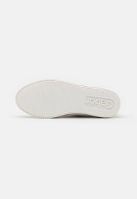 Suola di sneaker bianca con scanalature orizzontali e bordi arrotondati; presenta il logo del marchio in rilievo e un design minimalista.