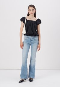Black puff-sleeve top, light blue flared jeans, black pointed-toe heels, holding a small white handbag with textured detail.