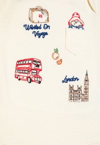 Kreemikangas, millel on kirjud tikandid: kohver, Paddingtoni karu, punane kahekorruseline buss, apelsin ja Big Ben koos tekstiga "London".
