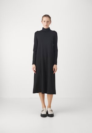 Musta pitkähihainen mekko, jossa on korkea kaula-aukko, valmistettu pehmeästä kankaasta. Mekko ulottuu pohkeeseen saakka ja siinä on rento malli.