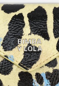 Żółty portfel z czarnym, plamkowanym wzorem, z teksturowaną powierzchnią, srebrnym logo "BIMBA Y LOLA" oraz jasnosłonecznymi wykończeniami.