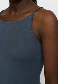 Haut sans manches en maille côtelée bleu foncé, présentant un col arrondi et une coupe ajustée, avec une surface lisse et texturée.