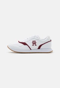 Sneakers z białą syntetyczną cholewką, burgundowymi zamszowymi akcentami, wyściełanym kołnierzem, teksturowanymi panelami oraz gumową podeszwą z trójkątnym wzorem bieżnika.