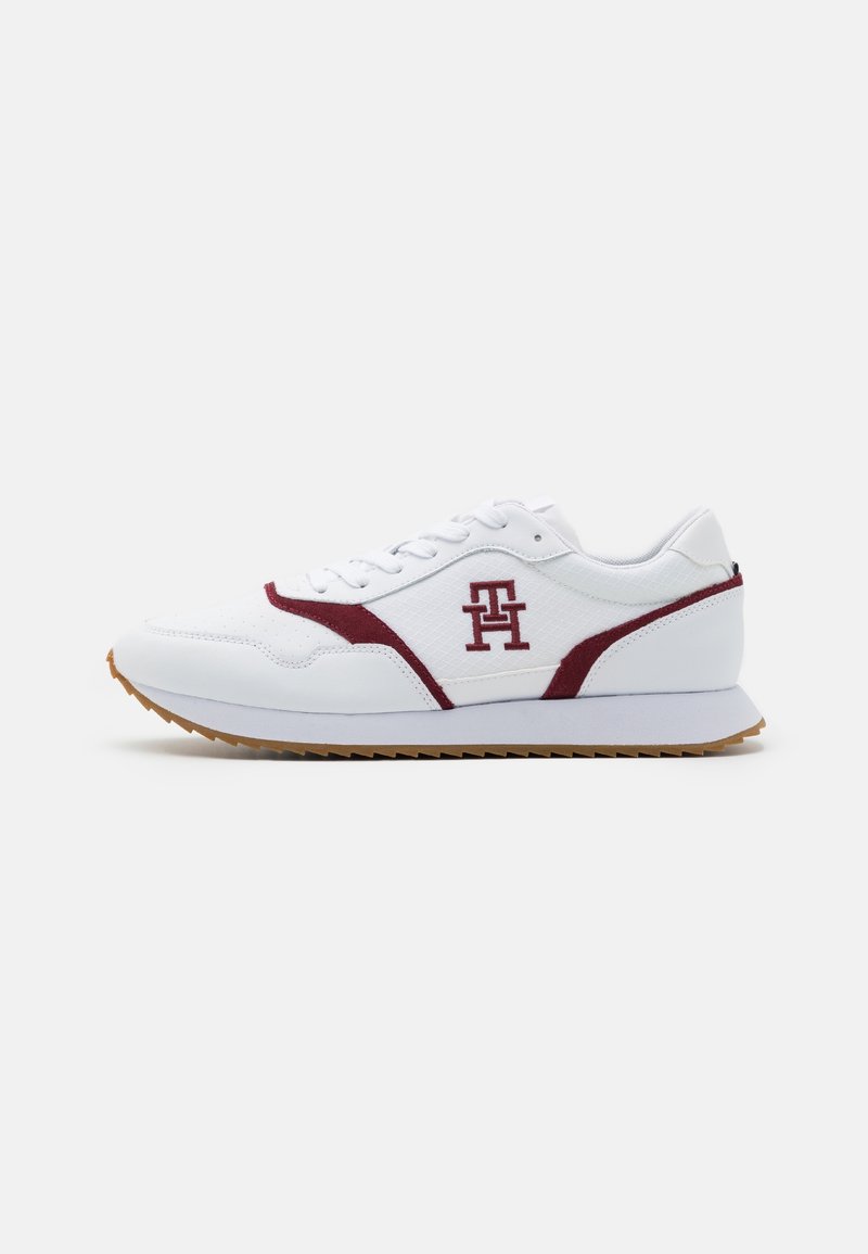 Sneakers z białą syntetyczną cholewką, burgundowymi zamszowymi akcentami, wyściełanym kołnierzem, teksturowanymi panelami oraz gumową podeszwą z trójkątnym wzorem bieżnika.