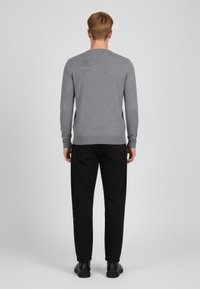 Grå långärmad stickad tröja med rund halsringning; bärs med svarta byxor och svarta skor, sedd bakifrån. Slät textur.