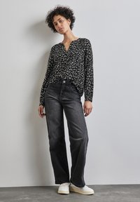 Blusa leopardata nera e crema con maniche lunghe e scollatura a V, abbinata a jeans grigi scuri a vita alta e sneakers bianche.