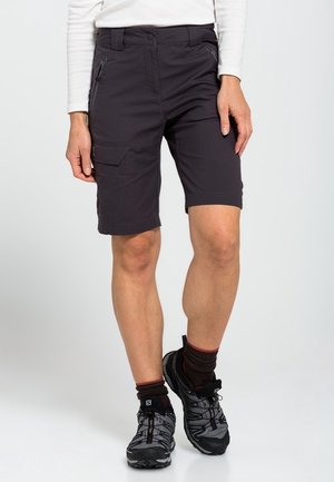 Person wearing black knee-length cargo shorts, black hiking shoes, and dark socks, standing with one leg slightly crossed.