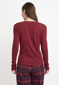 Top de manga larga burdeos con un patrón texturizado, escote redondo y corte relajado. Presenta mangas ajustadas y un dobladillo recto.