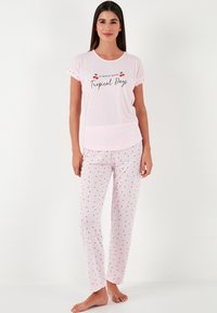 Light pink cotton pajama set featuring a t-shirt with "Tropical Days" print and patterned pants with small red cherry motifs.