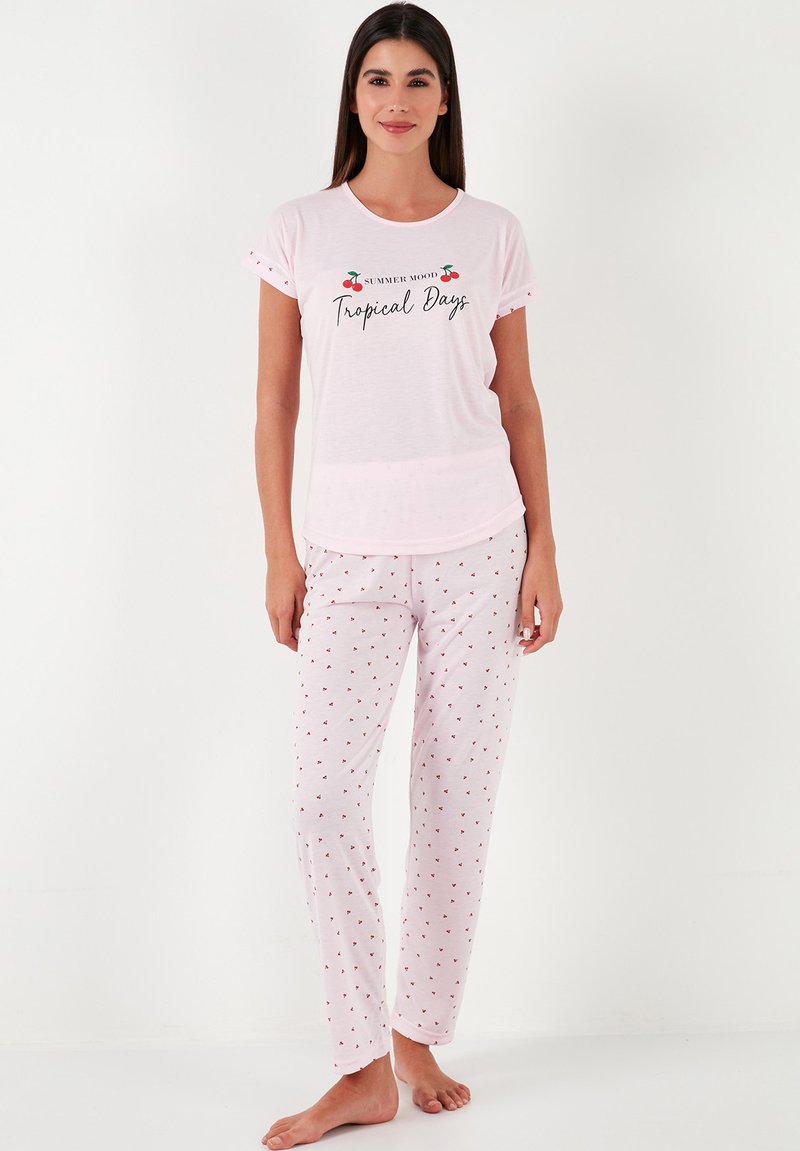 Light pink cotton pajama set featuring a t-shirt with "Tropical Days" print and patterned pants with small red cherry motifs.