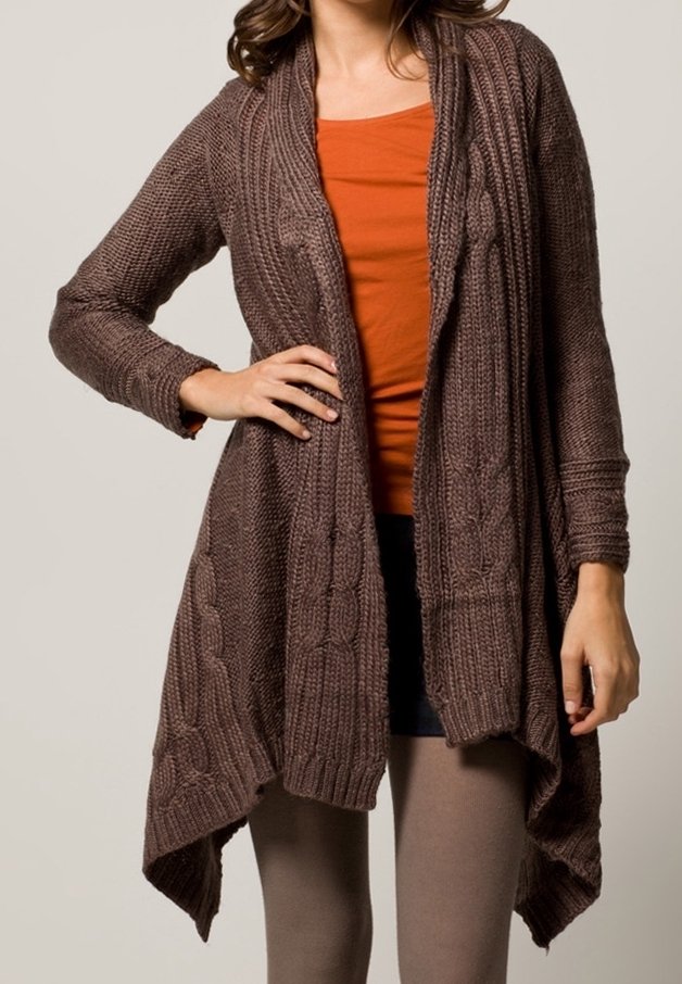 Brun stickad cardigan med kabelmönster, öppen fram, och långa ärmar. Strukturerad, något längre bak, bärs över en orange topp.
