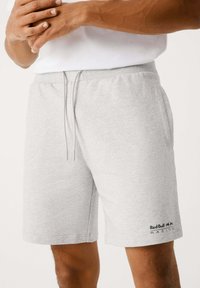 Pantalones cortos deportivos grises hechos de tela suave, con una cintura elástica y cordón, bolsillos laterales y un logo en la parte inferior de la pierna izquierda.