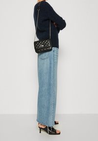 Prošívaná černá kožená crossbody taška se stříbrným kováním, nošena s tmavě modrým svetr a světle modrými širokými džíny se třepeným lemem.