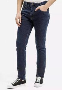 Ciemnoniebieskie slim-fit dżinsy wykonane z denimu, z pięcioma kieszeniami, zapinane na guzik, noszone z czarno-białymi sneakersami.