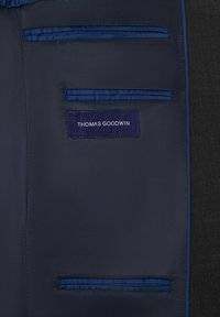 Doublure intérieure bleu marine avec deux poches plates et une étiquette portant l'inscription "THOMAS GOODWIN". Couture contrastée en bleu plus clair. Tissu extérieur texturé sombre.