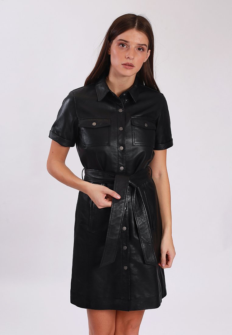 Czarna skórzana sukienka koszulowa z krótkimi rękawami, zapięciem na guziki, dwiema kieszeniami na piersi i pasującym paskiem w talii. Gładka tekstura.