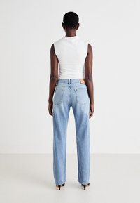Jeans de mezclilla azul con un corte relajado, cinco bolsillos y una etiqueta de marca marrón en la cintura trasera. La parte superior es una camisa sin mangas blanca ajustada.