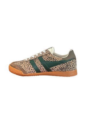 Zapatilla baja con patrón manchado en tonos beige y negro, franjas laterales verde oscuro, cordones blancos, puntera marrón y suela de goma naranja.