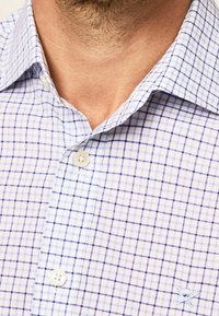 Blauw en wit geruit overhemd met een button-down kraag. Heeft kleine knopen en een lichtblauw geborduurd logo op de borst.