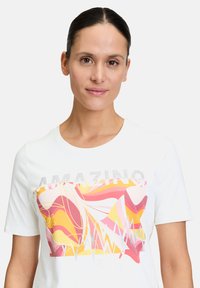 White short-sleeve t-shirt featuring a colorful abstract graphic with pink, yellow, and purple tones, and the word "AMAZING" in metallic accents.