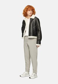 Zwarte leren cropped jas met witte schapenvacht voering, gecombineerd met lichtgrijze broeken en witte sportschoenen. Model heeft golvend haar.