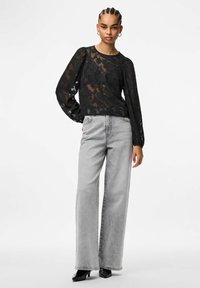 Juoda permatoma palaidinė su gėlių raštu, ilgomis rankovėmis ir apvalia iškirpte, derinama su pilko džinso plačiomis, aukštas liemuo kelnių kojomis. Juodi aukštakulniai.